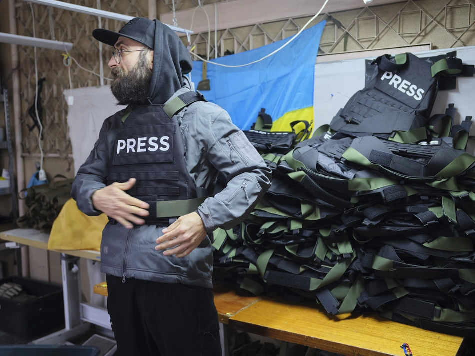 Ein Mann legt sich in einer Werkstatt eine Weste mit der Aufschrift „PRESS“ an – Schutz für Medienschaffende, die im Ukrainekrieg verlässliche Informationen für die Bevölkerung bereitstellen.