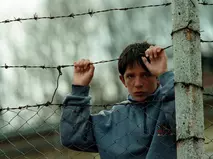Kosovo-Krieg 1999: Auswirkungen der Humanitären Hilfe Ein Junge, der sich während des Kosovo-Konflikts 1999 an einem Stacheldrahtzaun festhält - Symbol für Not und Hoffnung, unterstützt von der Glückskette.