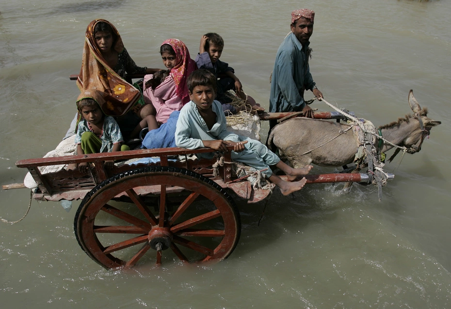 Ein Esel, der einen Wagen mit fünf Kindern zieht, während ein Mann neben ihm durch die überschwemmten Straßen läuft, während der humanitären Hilfsmaßnahmen während der Überschwemmungen in Pakistan 2010.