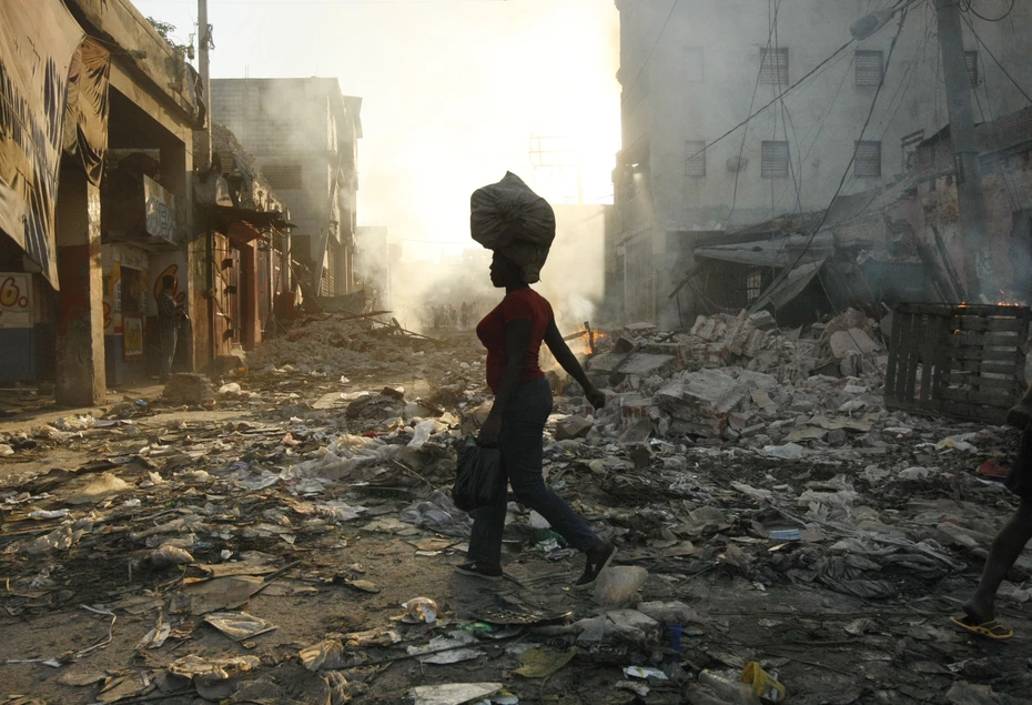 Eine Frau läuft bei Sonnenuntergang durch eine zerstörte Stadt in Haiti und trägt eine Tasche auf dem Kopf. Dies nach dem Erdbeben 2010, das die Glückskette mit ihrer Hilfe unterstützt hat.