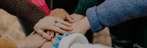 Mehrere Hände liegen übereinander – ein Symbol für Solidarität, Gemeinschaftsspenden und gemeinsame Hilfe.