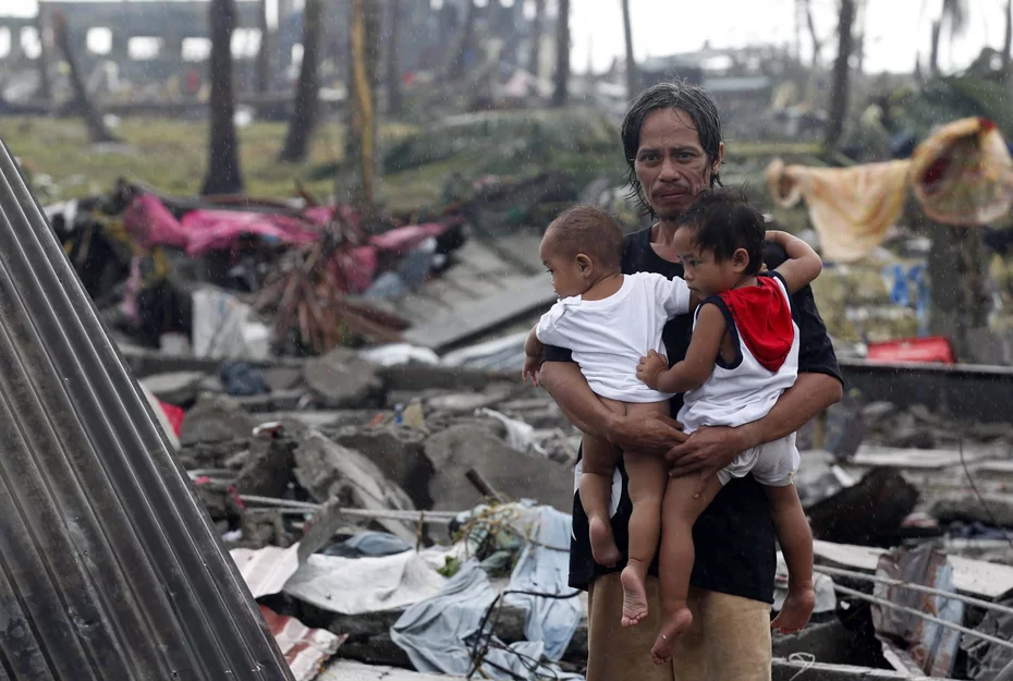 Ein Mann, der inmitten der Zerstörung durch den Taifun Haiyan im Jahr 2013 zwei Kinder im Arm hält, lächelt und zeigt damit seine Widerstandsfähigkeit und Hoffnung.