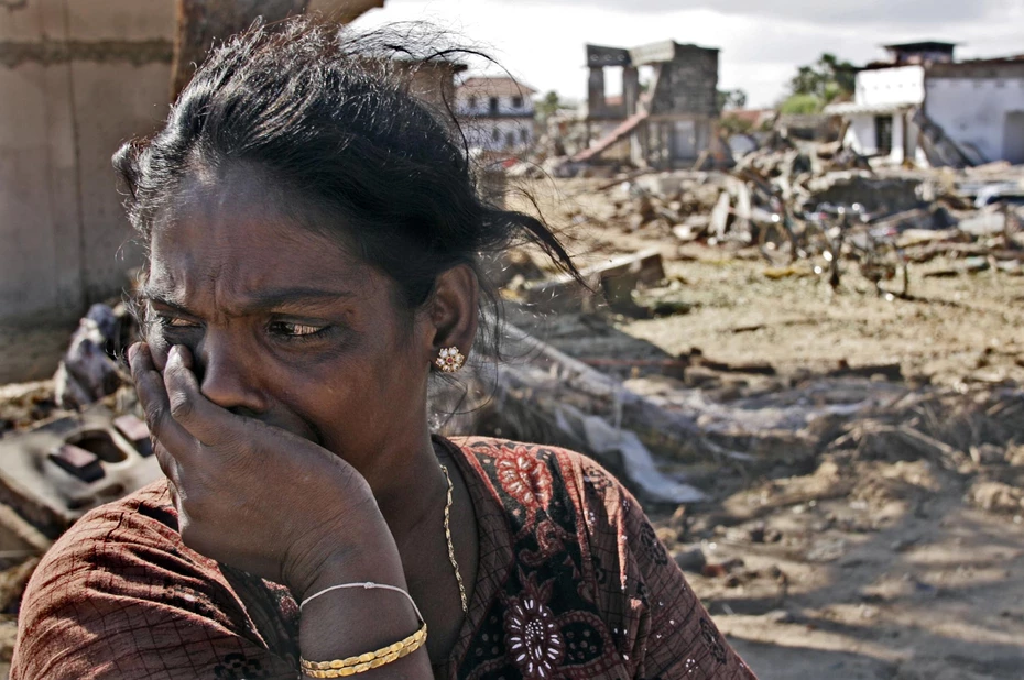 Eine Frau mit Tränen in den Augen schaut zur Seite, als sie nach dem Tsunami 2004 in Südostasien vor einer verwüsteten Landschaft steht.