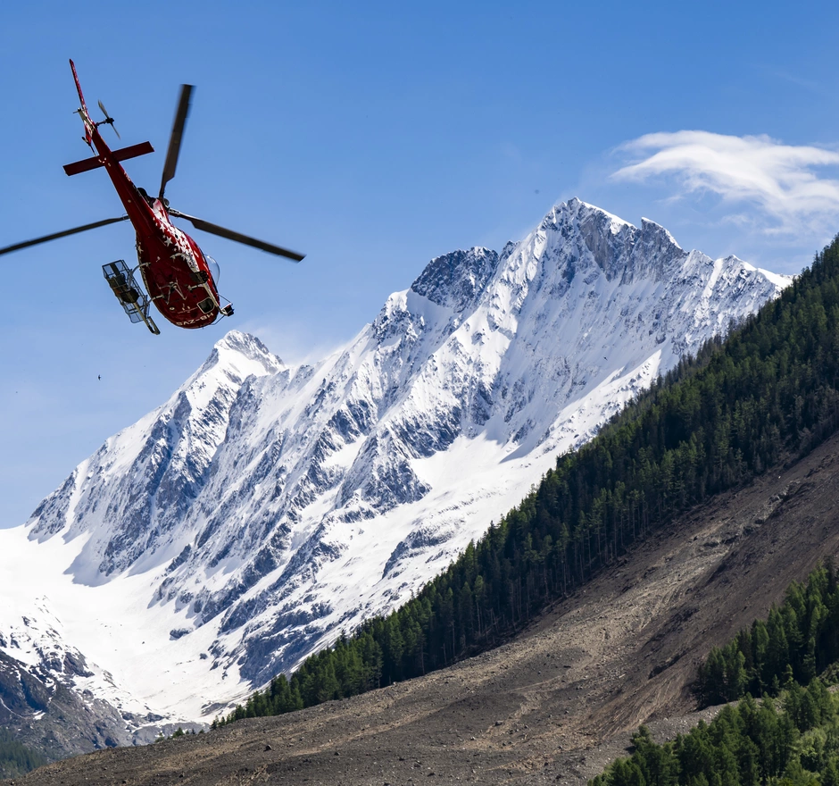 Rettungshubschrauber im Einsatz über dem Erdrutschgebiet von Blatten – dringende Spende für schnelle Nothilfe.