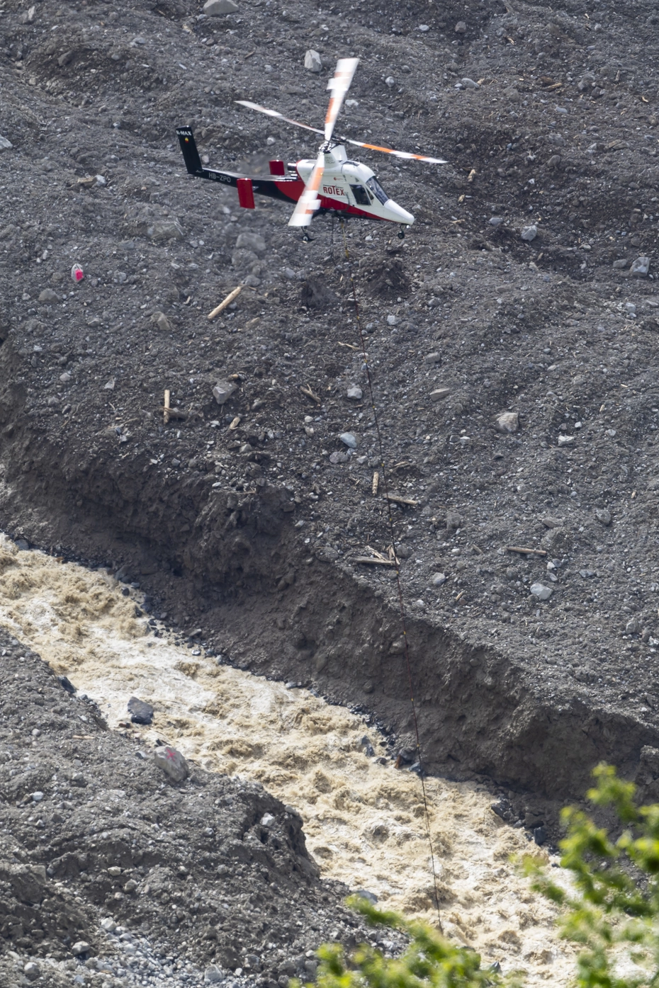 Helikopter im Einsatz über Geröll und Wildbach in Blatten – schnelle Hilfe nach Erdrutsch, Spenden dringend benötigt.